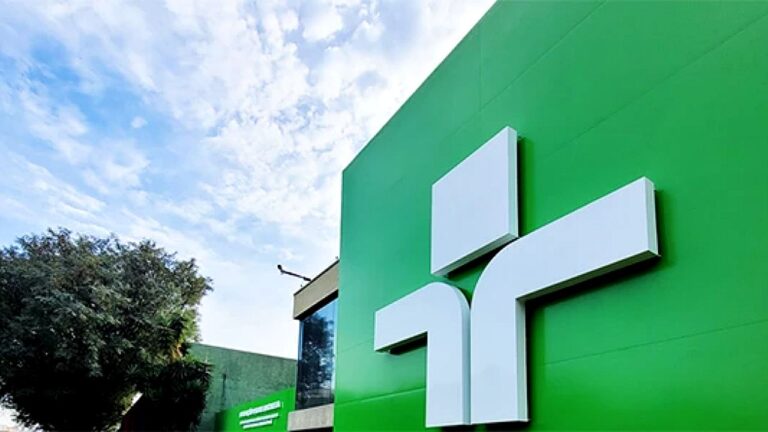 Logotipo da TV Cultura em fachada verde da emissora com céu azul ao fundo e área externa do prédio visível