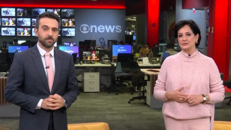 Victor Boyadjian e Monica Waldvogel apresentam telejornal da GloboNews em estúdio com redação e monitores ao fundo