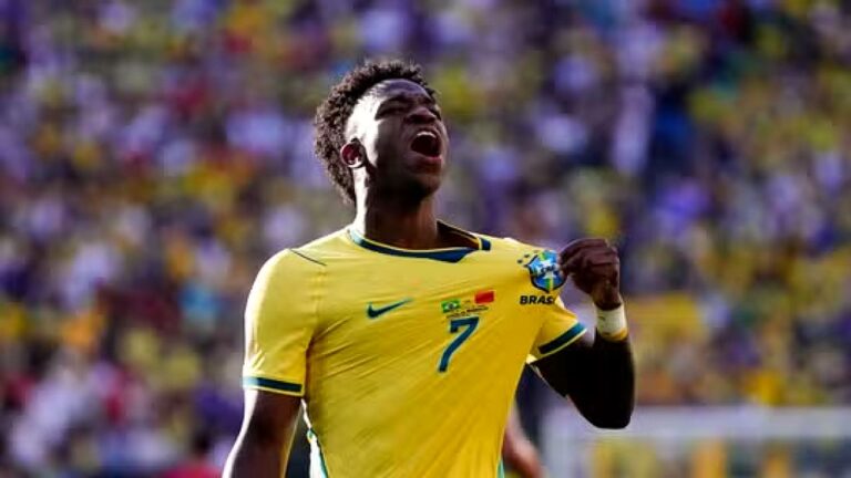 Vinícius Júnior comemora gol pela seleção brasileira enquanto segura o escudo da camisa em partida oficial do Brasil
