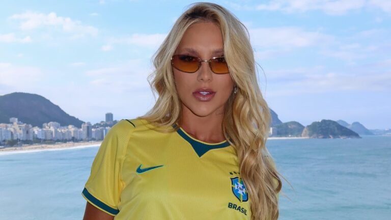 Virginia Fonseca usa camisa da seleção brasileira e óculos escuros diante da praia de Copacabana com o mar ao fundo no Rio de Janeiro