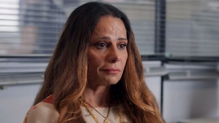Viviane Araujo com olhar emocionado em cena de novela ambientada em escritório com persianas ao fundo
