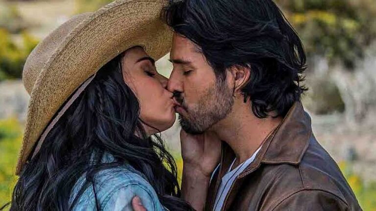 Protagonistas trocam beijo em cena da novela A Desalmada ao ar livre com chapéu e jaqueta de couro