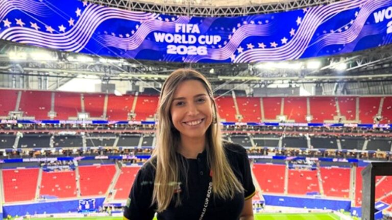 Alinne Fanelli sorri em estádio durante cobertura da Copa do Mundo de 2026 com telão da FIFA ao fundo