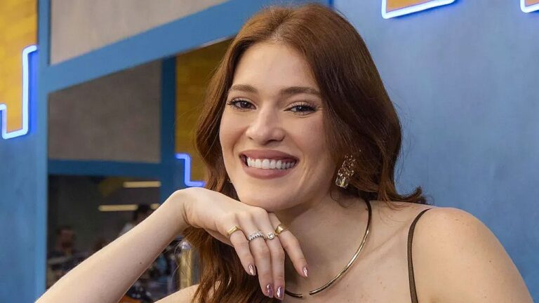Ana Clara sorri apoiando o rosto na mão durante participação em programa de televisão em estúdio