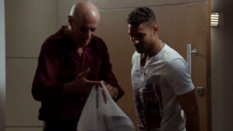 Ator entrega uma sacola a Jorginho (Cauã Reymond) em cena da novela Avenida Brasil