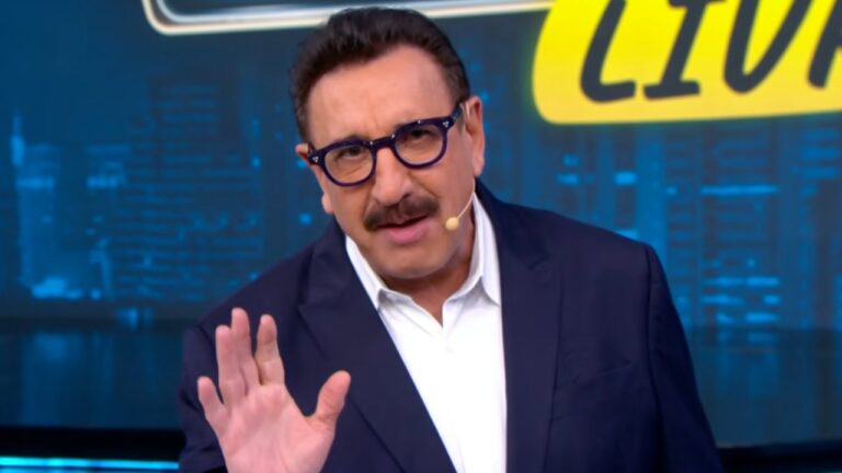 Carlos Massa Ratinho de terno azul e camisa branca faz gesto com a mão durante apresentação em estúdio de TV