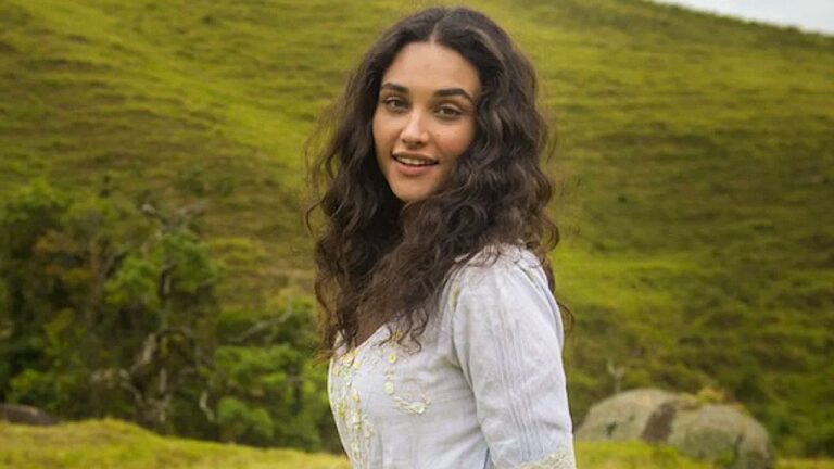 Débora Nascimento sorri em cenário rural durante cena da novela Êta Mundo Bom!