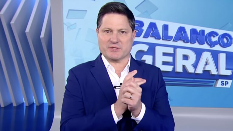 Eleandro Passaia, de terno azul, gesticula no estúdio do Balanço Geral SP, diante de painel do programa