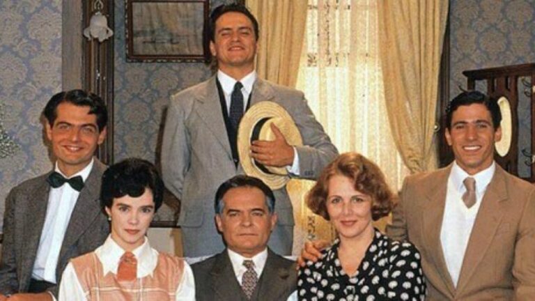 Elenco de Éramos Seis posa em sala de época com três homens em pé e três personagens sentados diante da janela