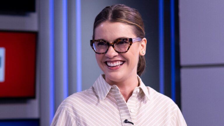 Elisa Veeck, usando óculos e sorrindo com camisa listrada clara, no estúdio da CNN Brasil