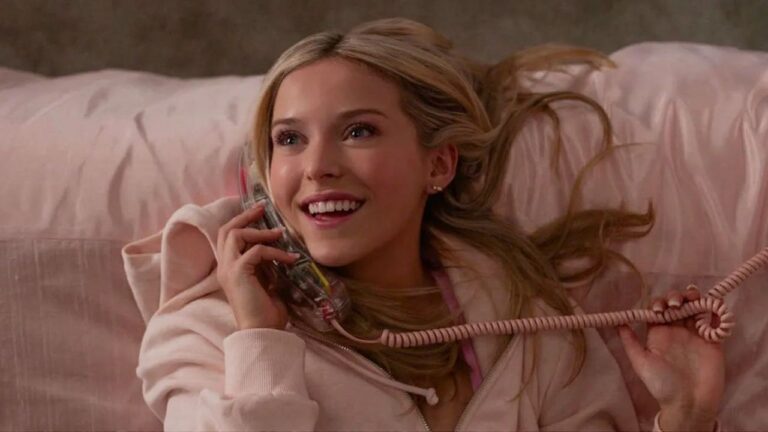 Elle sorri enquanto fala ao telefone deitada na cama em cena da série Elle