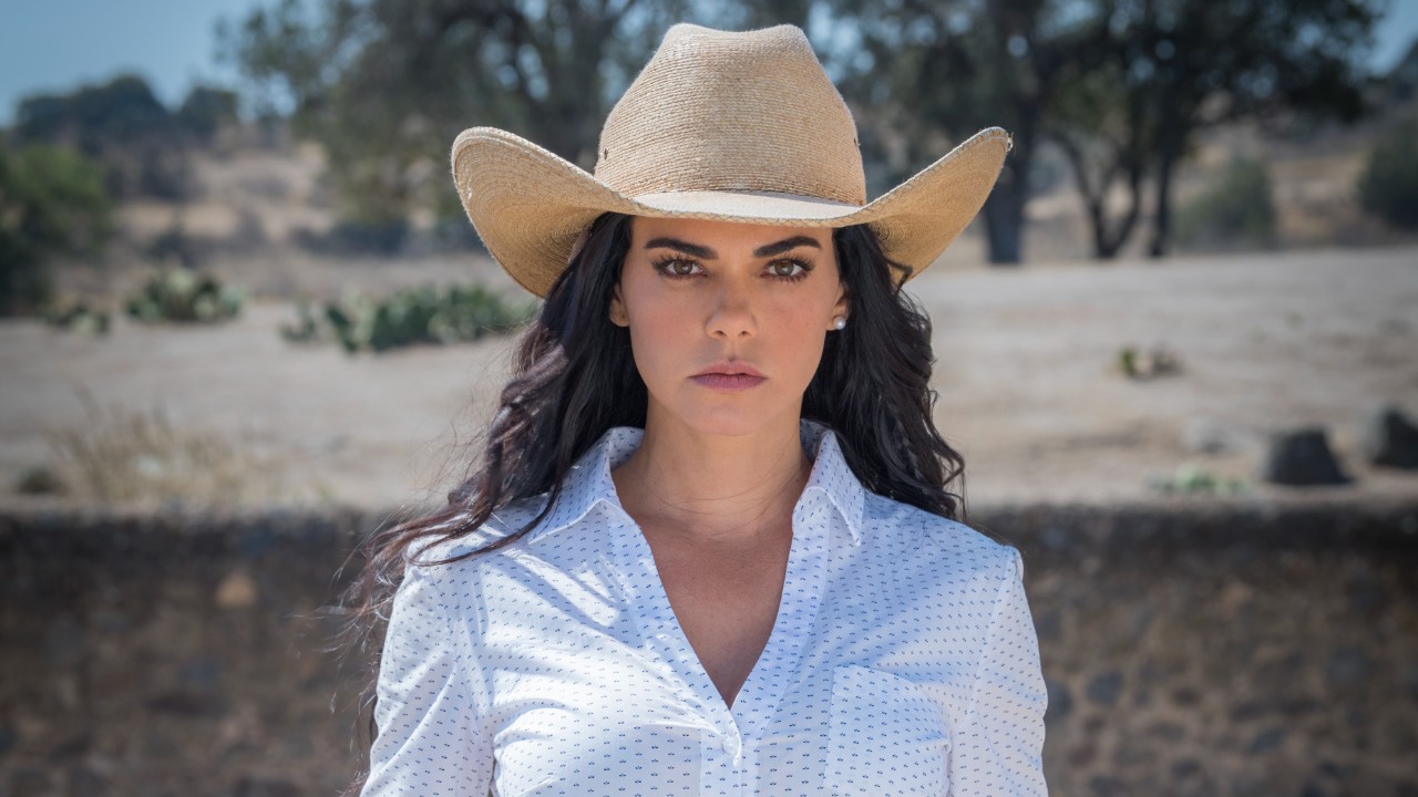 Fernanda (Livia Brito) de chapéu e camisa branca encara a câmera em cenário rural árido na novela A Desalmada