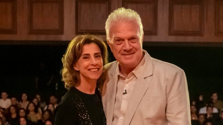 Fernanda Torres e Pedro Bial sorrindo lado a lado diante de plateia em teatro