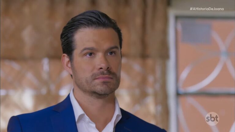 Gabriel, de blazer azul e camisa branca, com expressão séria em cena de A História de Joana