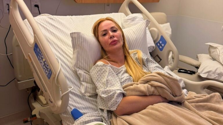 Ju Isen deitada em cama de hospital, veste roupa hospitalar e está coberta por manta em quarto de internação