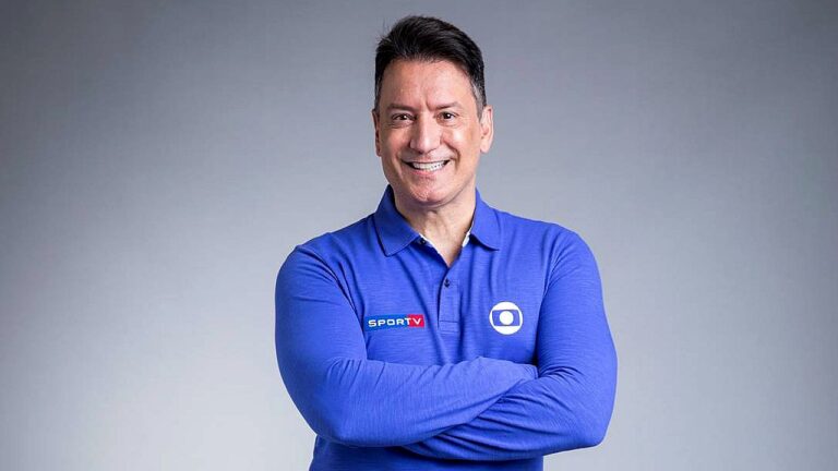 Luiz Carlos Jr. sorri com braços cruzados usando camisa da Globo e do sportv em foto promocional da emissora