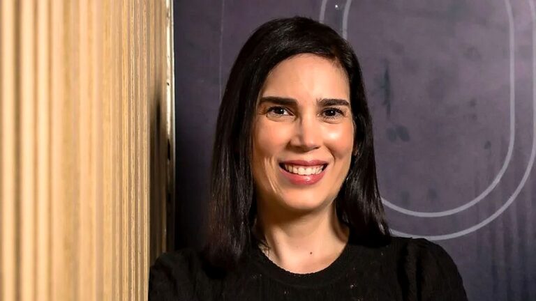 Marília Toledo sorri diante da câmera em retrato com blusa preta e fundo interno desfocado