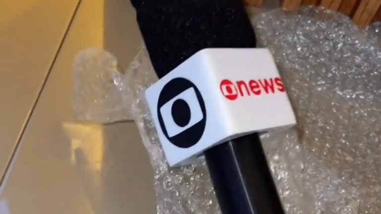 Microfone da GloboNews com logotipo da Globo apoiado sobre plástico-bolha em superfície clara