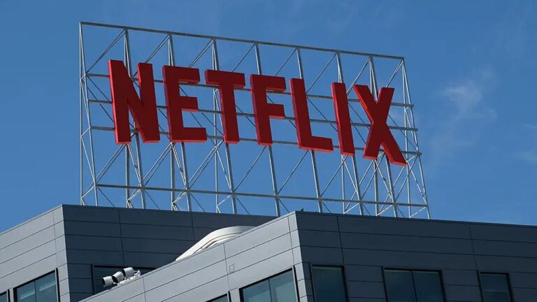 Logotipo da Netflix em letras vermelhas instalado no topo de prédio corporativo sob céu azul