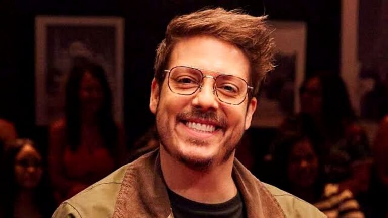 Fábio Porchat sorri usando óculos durante gravação de programa de entrevistas com plateia ao fundo