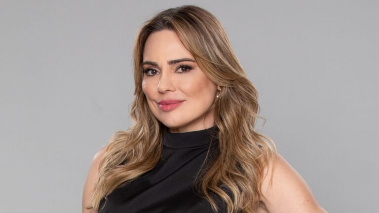 Rachel Sheherazade de cabelo loiro ondulado e blusa preta posa para retrato com fundo cinza