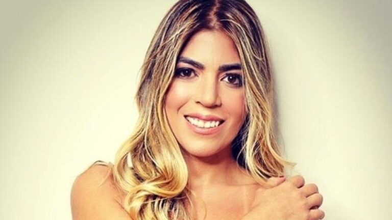 Raquel Pacheco sorri para a câmera em retrato com cabelo loiro ondulado e fundo claro desfocado