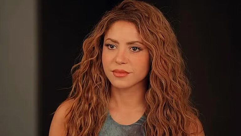 Shakira com cabelo cacheado e expressão séria em cena de série dramática durante conversa dentro de casa