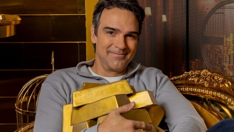 Tadeu Schmidt sorri enquanto segura barras de ouro sentado em poltrona dourada