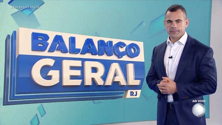 Tino Júnior, de blazer azul e camisa branca, diante do telão do Balanço Geral RJ