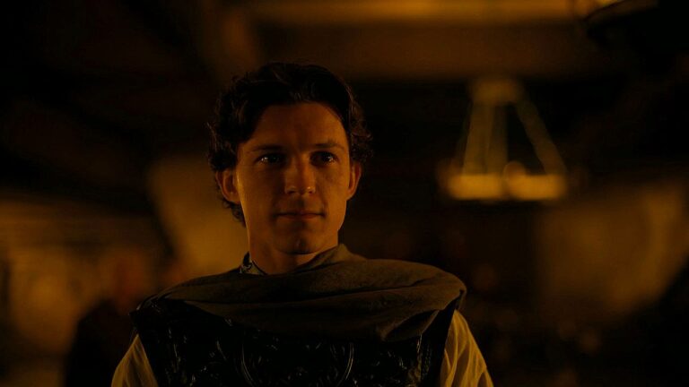 Tom Holland com armadura em cena de A Odisseia dentro de ambiente iluminado por luz baixa