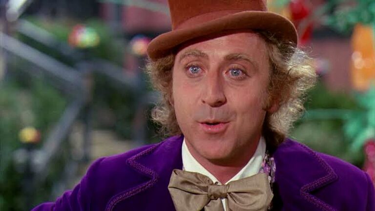 Willy Wonka com cartola marrom e casaco roxo em cena clássica de A Fantástica Fábrica de Chocolate