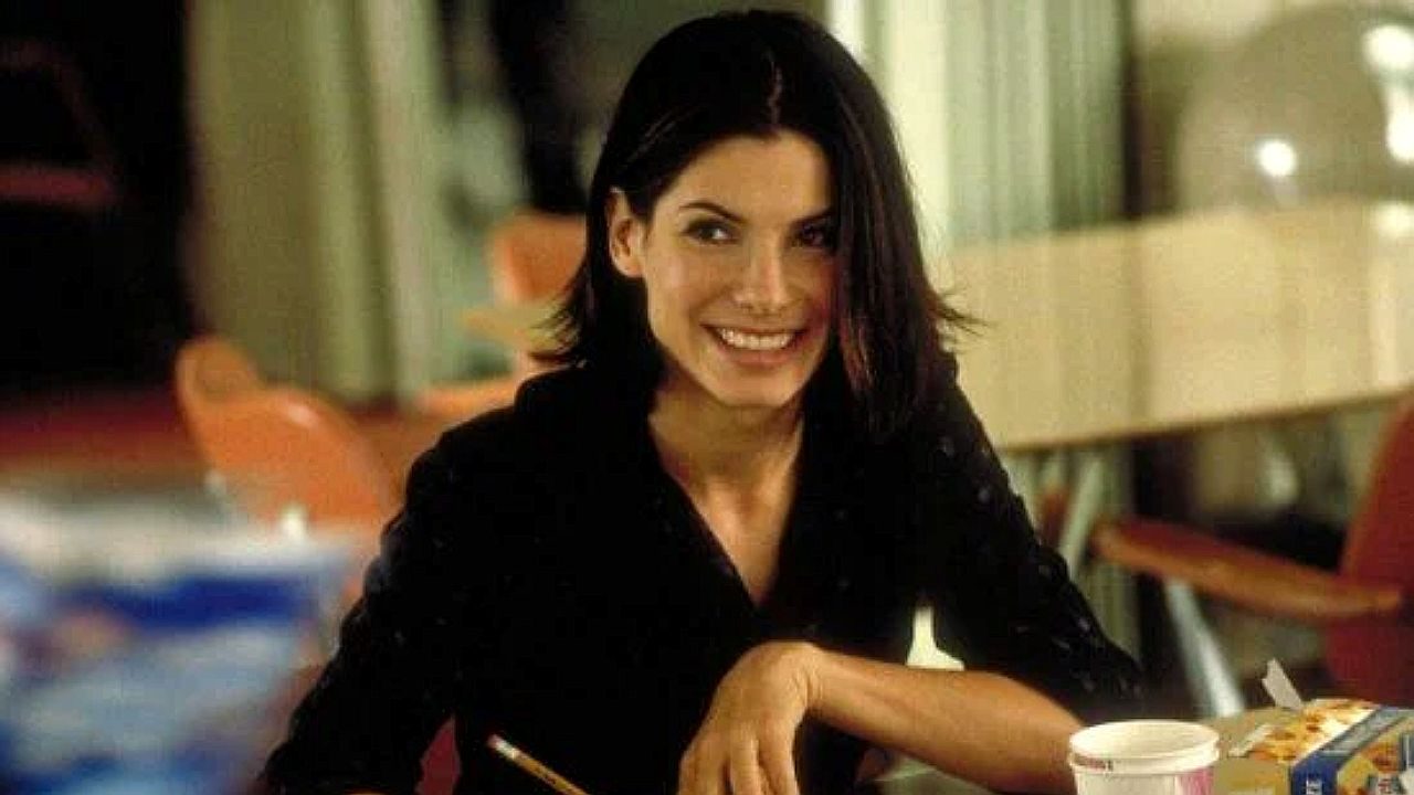 Mulher sorri enquanto segura hashis sentada à mesa em restaurante em cena de filme