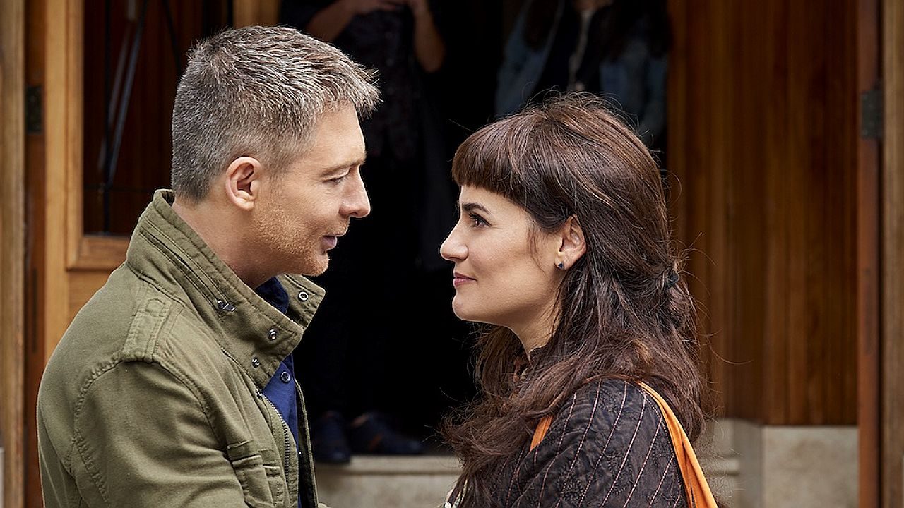 Homem e mulher se encaram próximos em cena romântica em frente a porta de madeira