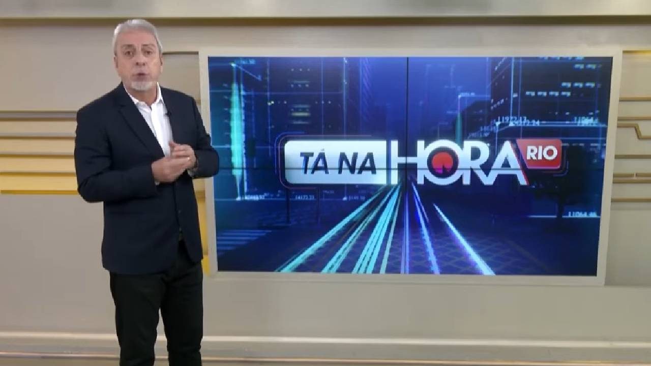 Clóvis Monteiro em pé no estúdio ao lado do telão com o logo do Tá na Hora Rio do SBT