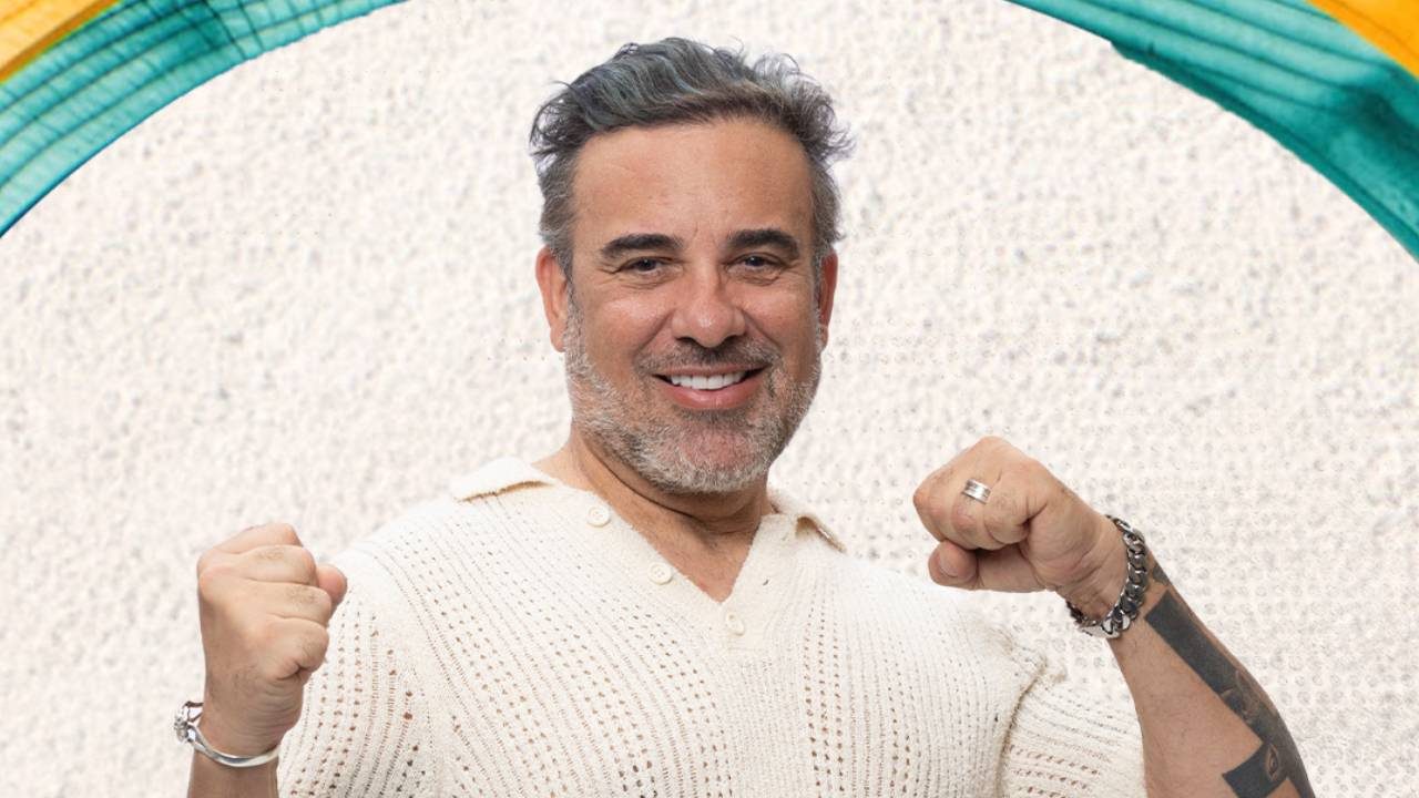 Fabiano Morais com cabelo grisalho e suéter de tricô sorrindo e levantando os punhos em gesto de vitória