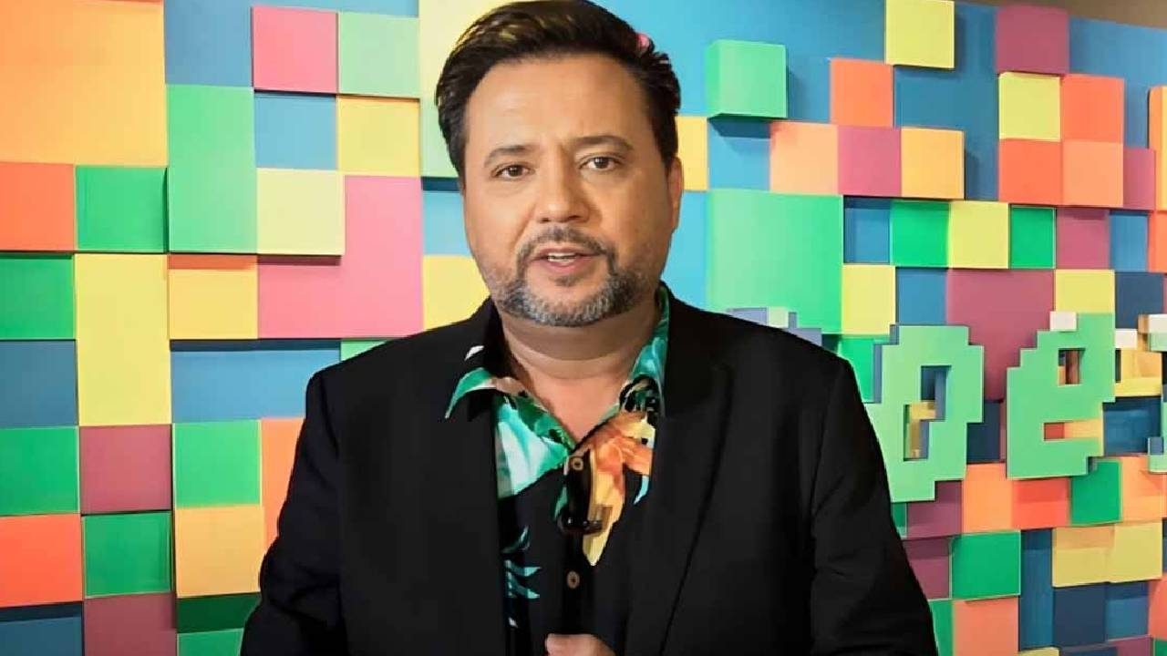 Geraldo Luís de blazer preto e camisa estampada em frente a painel colorido com blocos 3D