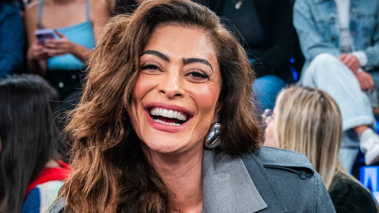 Juliana Paes sorri com expressão alegre usando casaco cinza e brinco prateado enquanto participa do programa Altas Horas com plateia ao fundo