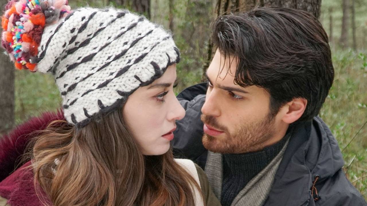 Özge Gürel com gorro de pompom e Can Yaman se olhando em cena romântica de inverno na novela Dolunay