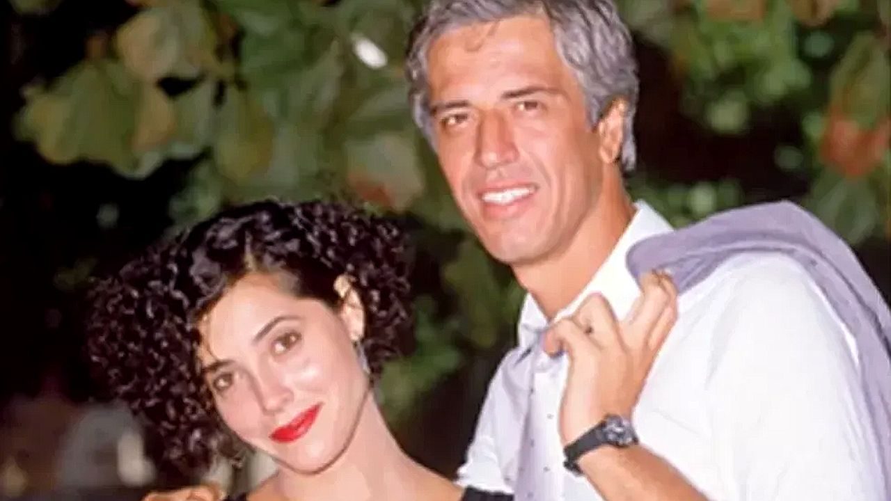Casal posa junto sorrindo em foto antiga ao ar livre com árvores ao fundo