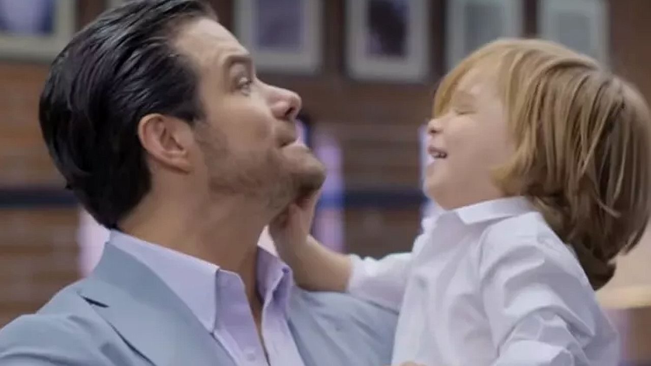 Homem segura criança ruiva no colo durante momento afetuoso em cena da novela A História de Joana