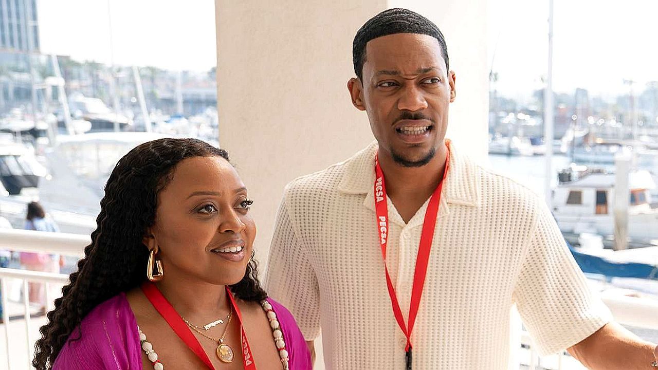 Casal com crachás observa algo surpreso em marina com barcos ao fundo durante evento ao ar livre