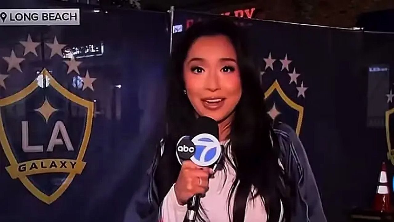 Repórter da ABC7 segura microfone durante entrada ao vivo em frente ao painel do LA Galaxy em Long Beach