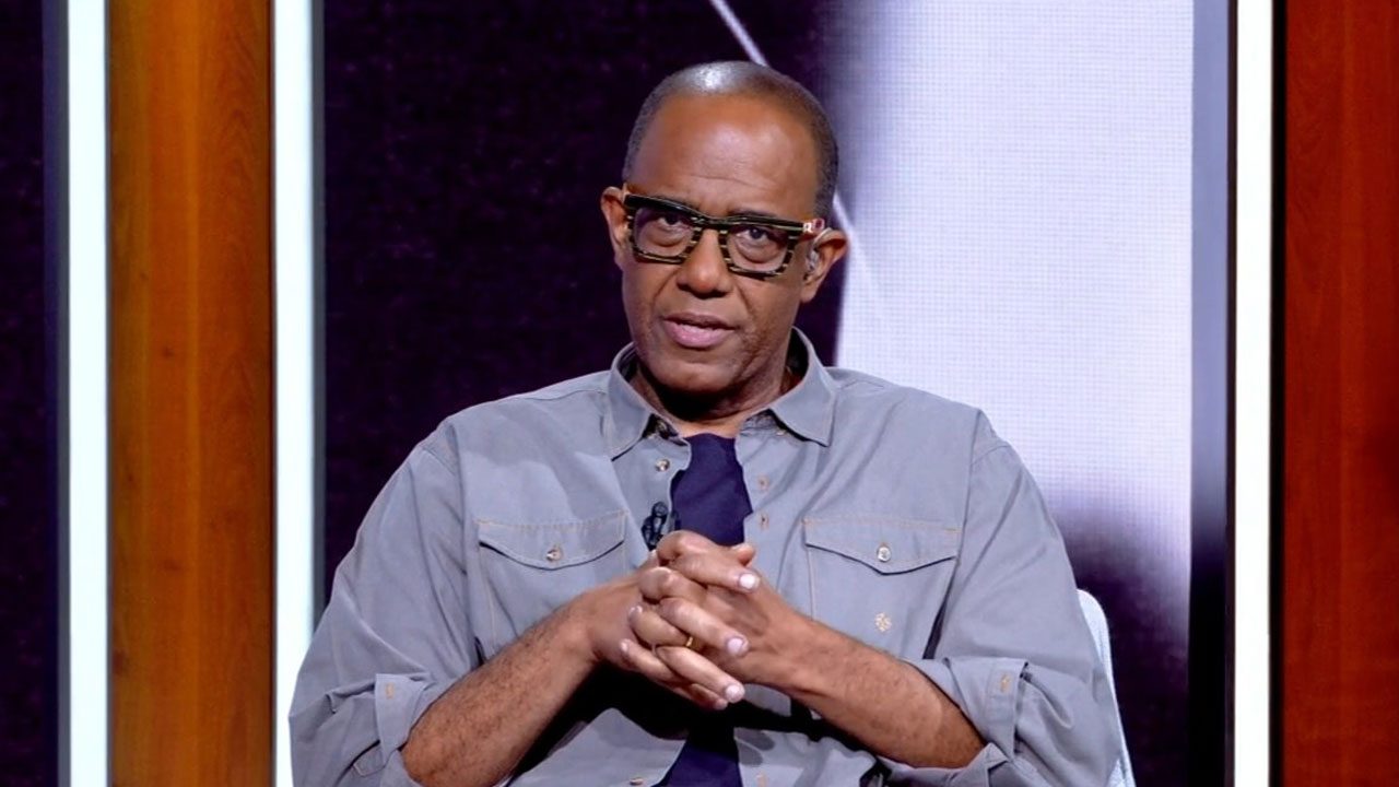 Jornalista e comentarista Abel Neto com óculos de aro escuro em plano médio, gesticulando com as mãos em programa de TV