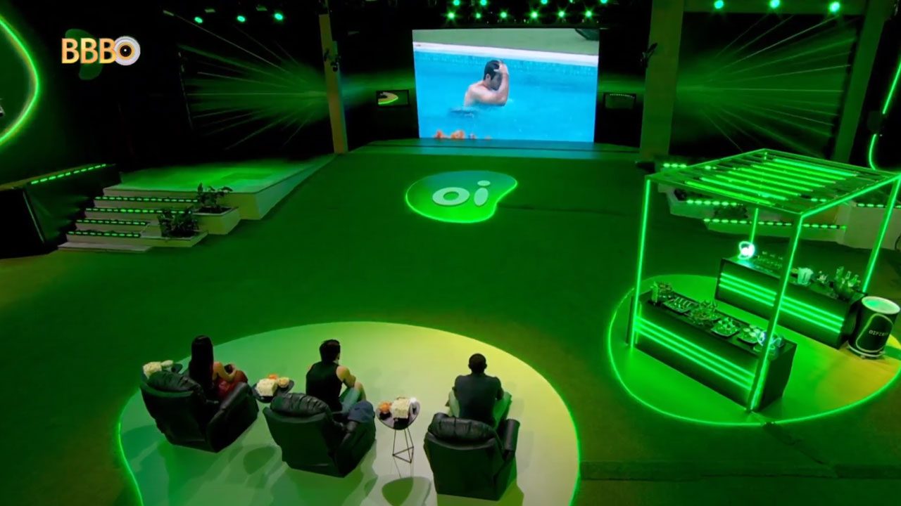 Cenário do BBB 24 com ação da Oi Fibra, três participantes assistem a vídeo em telão dentro da casa