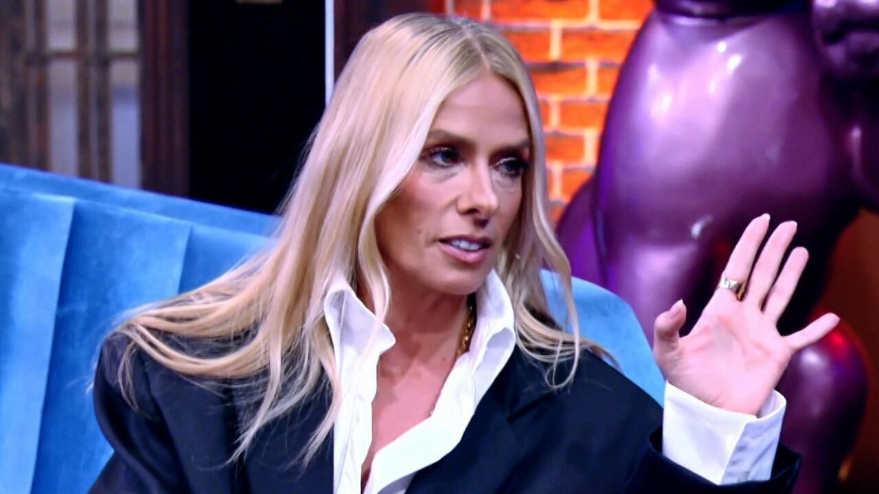 Adriane Galisteu sentada em sofá azul com camisa branca e blazer preto durante entrevista no Lady Night