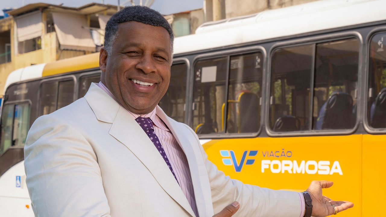 Ailton Graça caracterizado como Edson Bacelar em Volta por Cima da Globo em frente a ônibus da Viação Formosa
