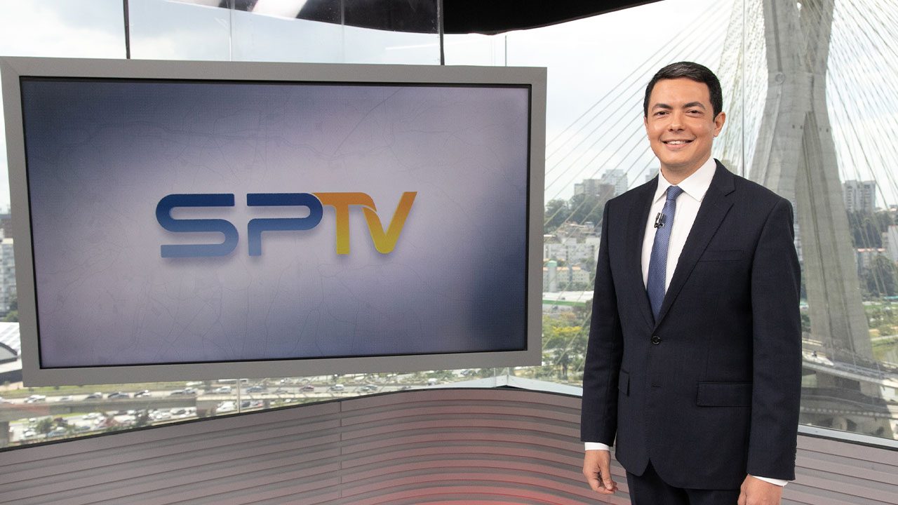 Alan Severiano de terno escuro e gravata azul apresentando o SP1 no estúdio da TV Globo em São Paulo