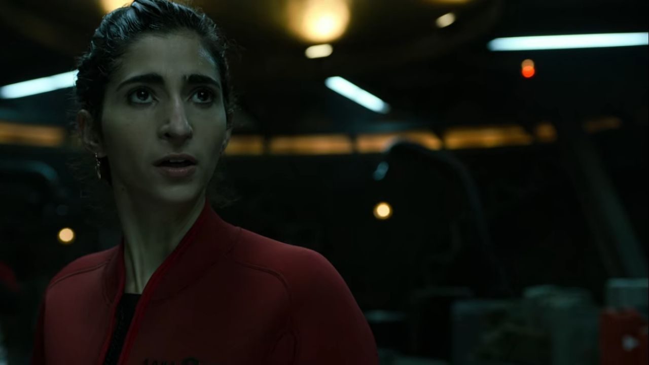 Mulher com expressão preocupada veste macacão vermelho em ambiente escuro e tecnológico, iluminado por luzes artificiais suaves