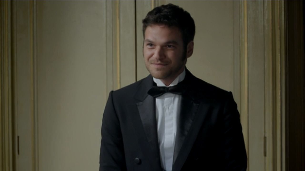 Ator usa smoking preto e sorri ao chegar para evento elegante em cena da novela Além do Tempo