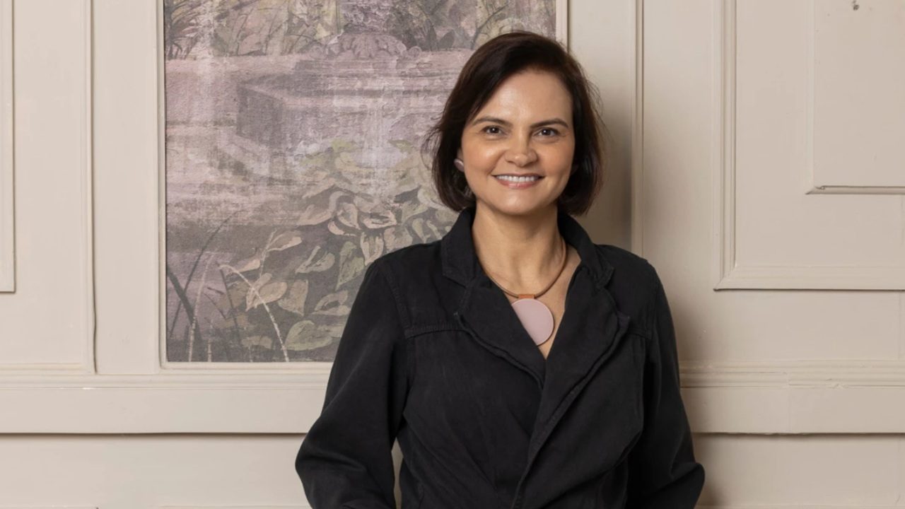 Mulher sorri para a câmera usando roupa preta em retrato profissional feito em ambiente interno com quadro decorativo ao fundo